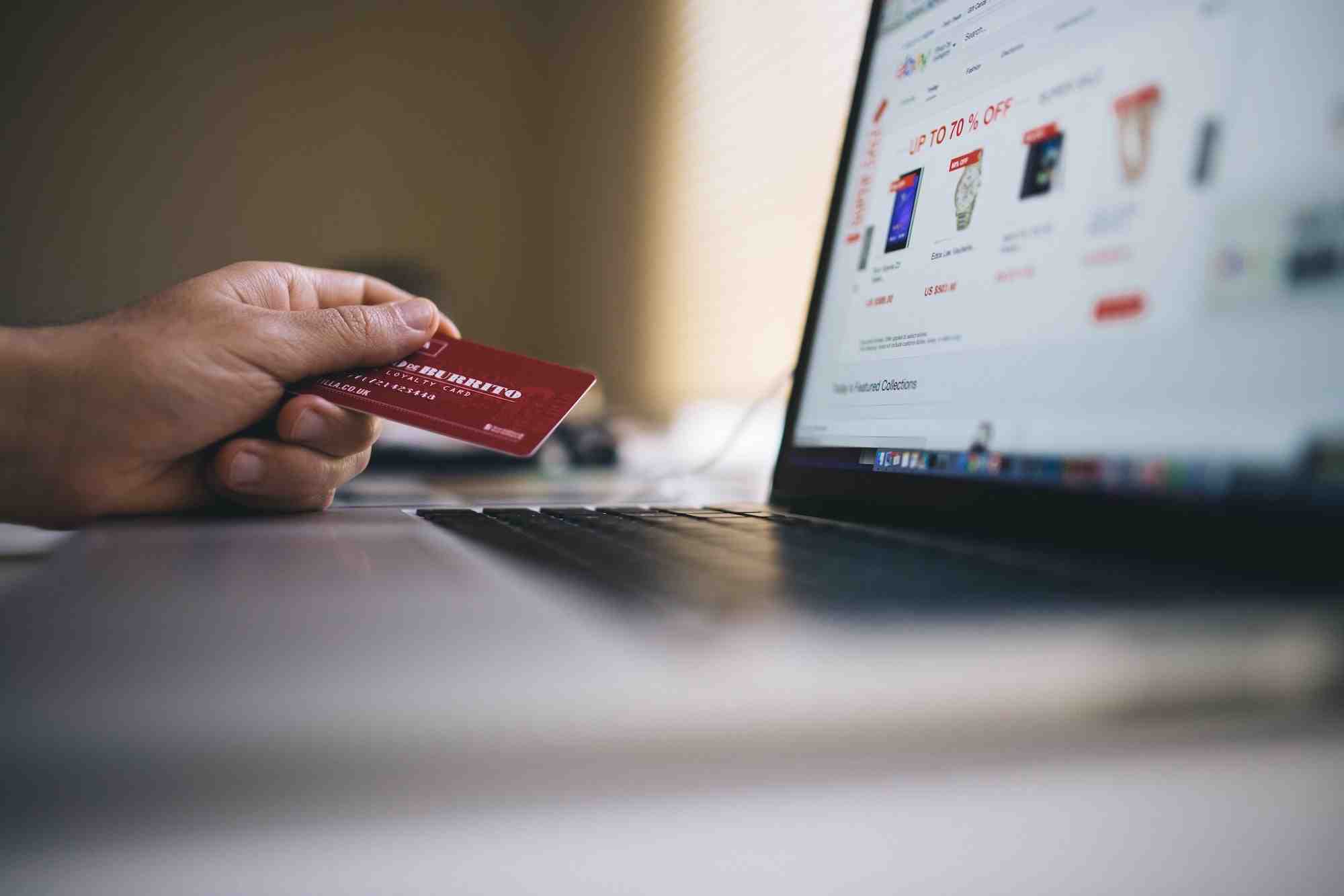 person holding a red card while shopping online using a laptop