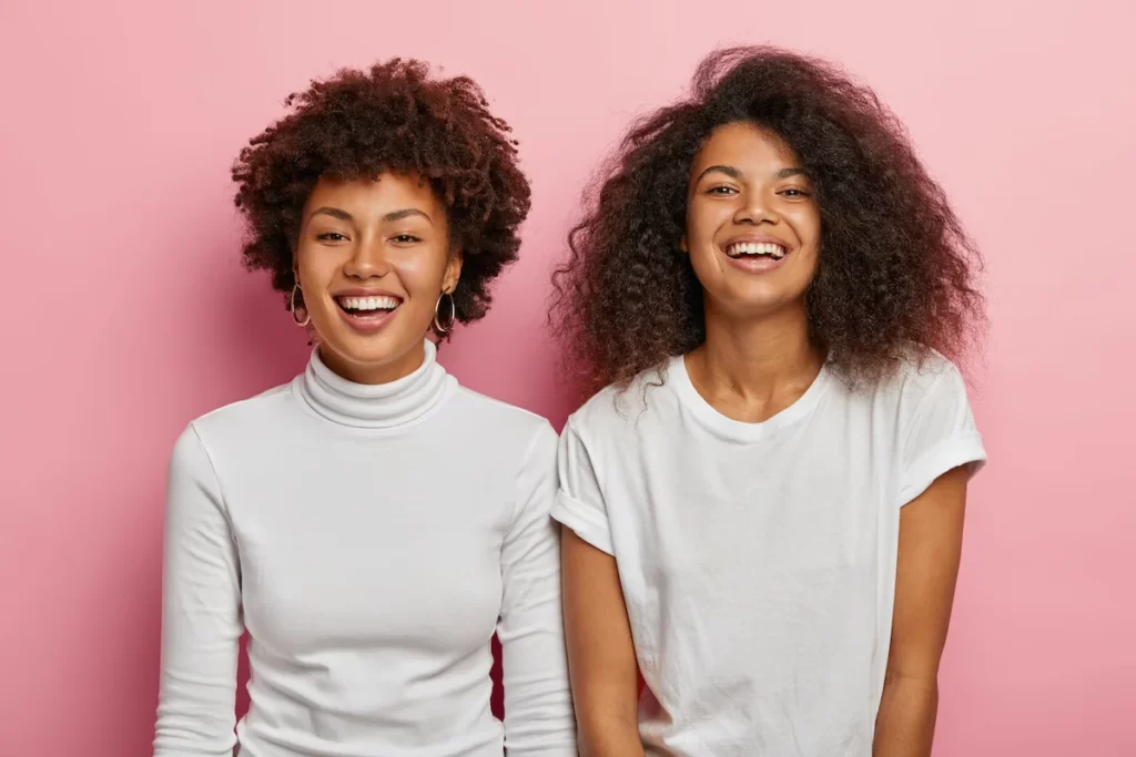 studio-shot-happy-afro-american-female-sisters-enjoy-good-moment-wear-white-casual-clothes-smile-broadly-have-fun-together-during-free-time-isolated-pink-wall (1)